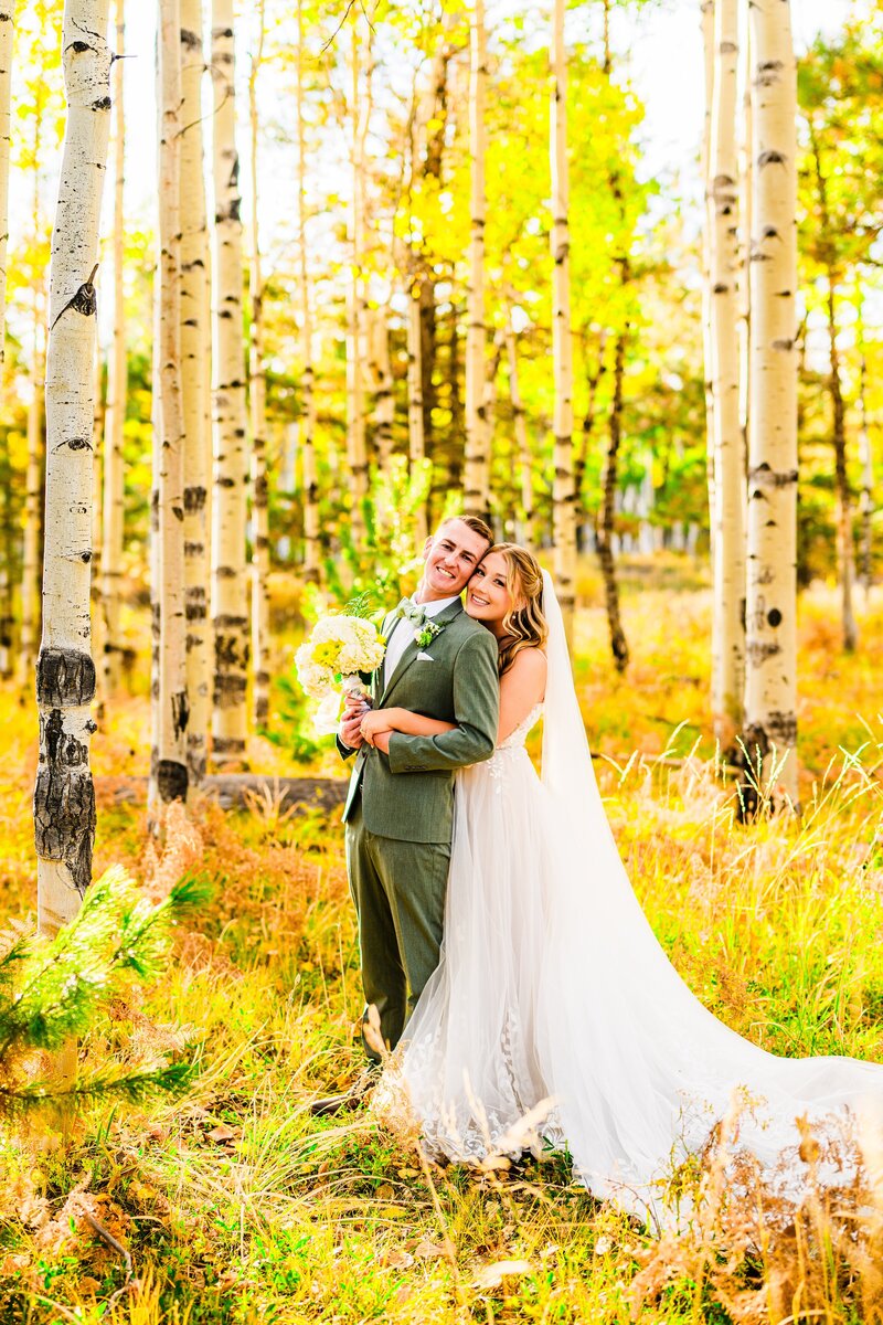 bride hugging groom from behind both smiling in wedding attire in golden fall aspen forest in Flagstaff wedding