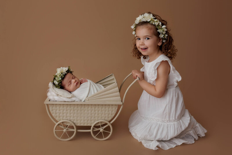 A newborn baby is peacefully sleeping, curled up on a soft, dusty rose-colored background. The baby is naked, showcasing their delicate, natural form with adorable baby rolls. A floral headband with pink and green flowers adorns the baby's head, adding a touch of sweetness to the serene scene. The baby's tiny hands are gently placed near their face, and their expression is calm and content, creating a heartwarming and tender portrait.