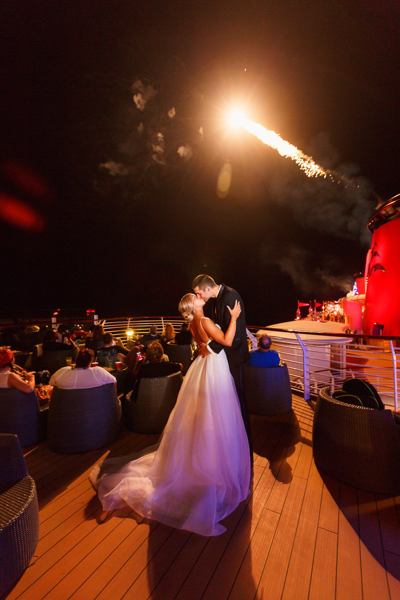 Bride and Groom kissing under fireworks on the deck of the Disney Dream