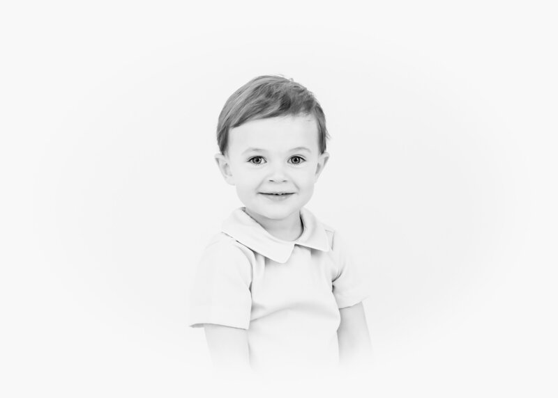Young boy smiling in a collared shirt against a white background.
