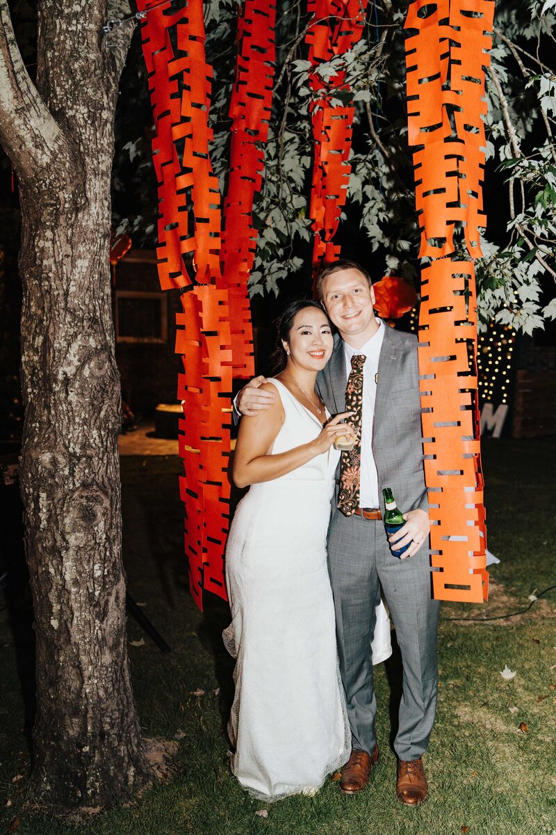 bride and groom surrounded by chinese paper decor hanging from a tree