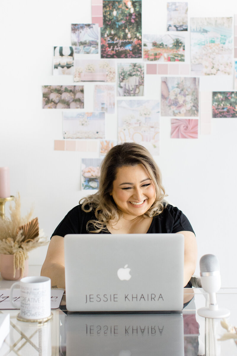 Jessie Khaira, luxury sikh wedding planner smiling at her desk looking at her laptop