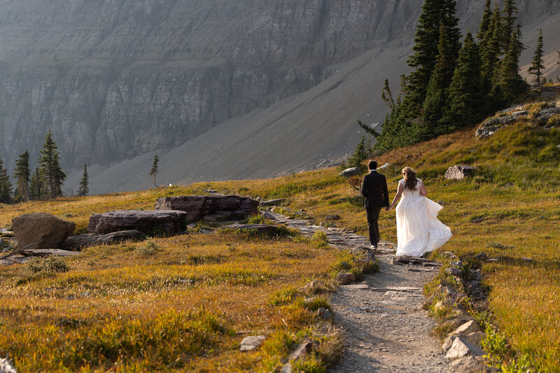 Bride and groom walking away down trail holding hands.