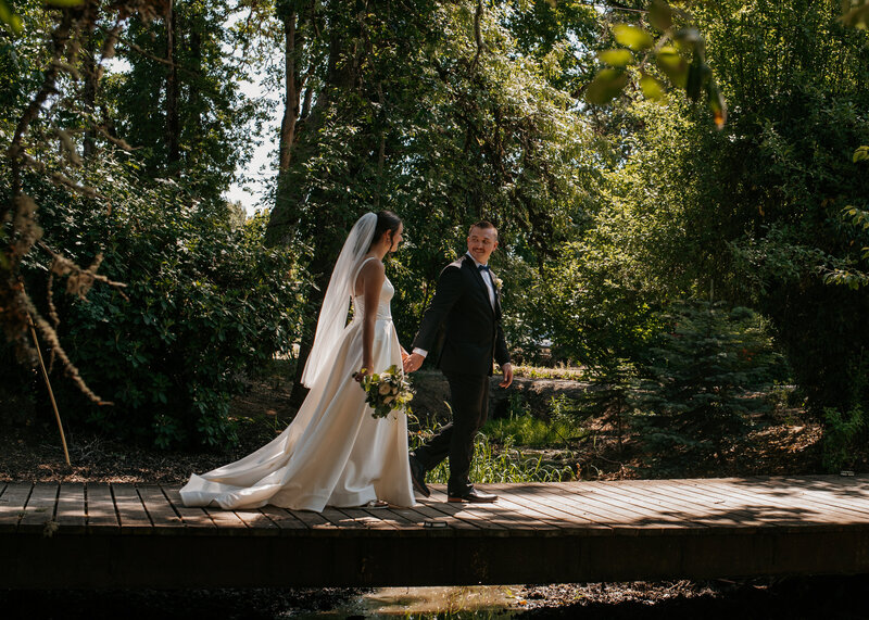 A happy couple strollling across the bridge at their garden wedding.