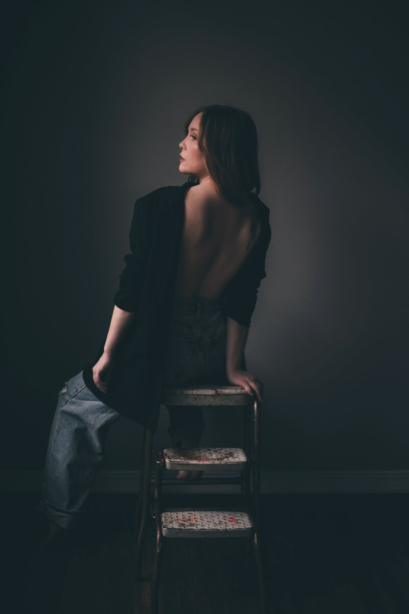 A woman sitting on a chair in a dark room, captured by an expert personal branding photographer in Shreveport Britt Elizabeth