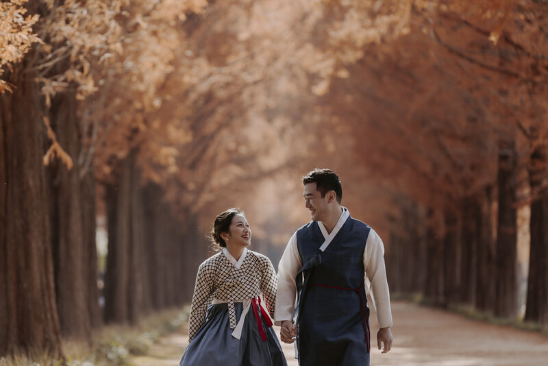 couple wearing white and blue hanboks walk down damyang metasequoia road during their prewedding shoot