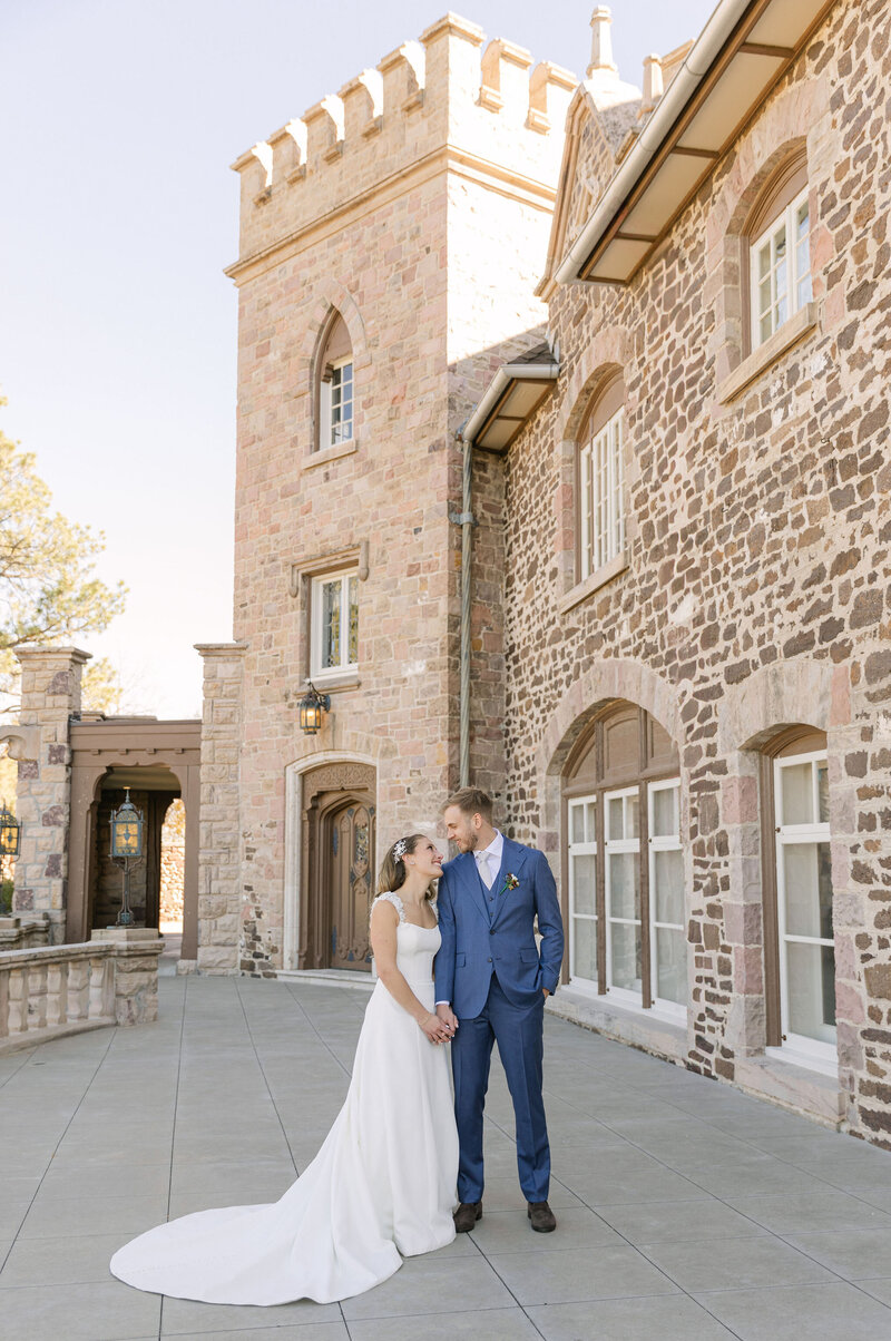 Bride and groom walking together in front of a historic stone estate called Highlands Ranch Mansion