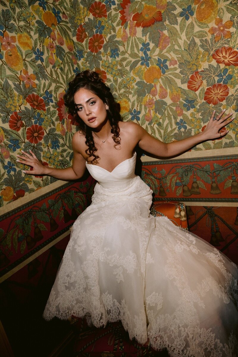 A bride with dark skin, wearing a white wedding gown and holding a bouquet of white flowers, gazes into the distance during her portrait session.