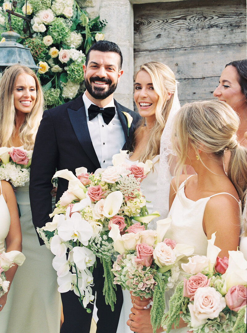 bride and groom laughing surrounded by wedding party