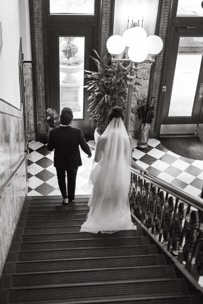 Bride and groom walking down grand staircase in historic venue with checkered floors