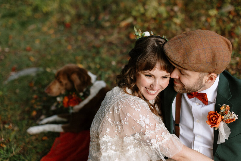 A couple in elegant wedding attire, surrounded by autumn foliage, sharing a tender moment together outdoors.