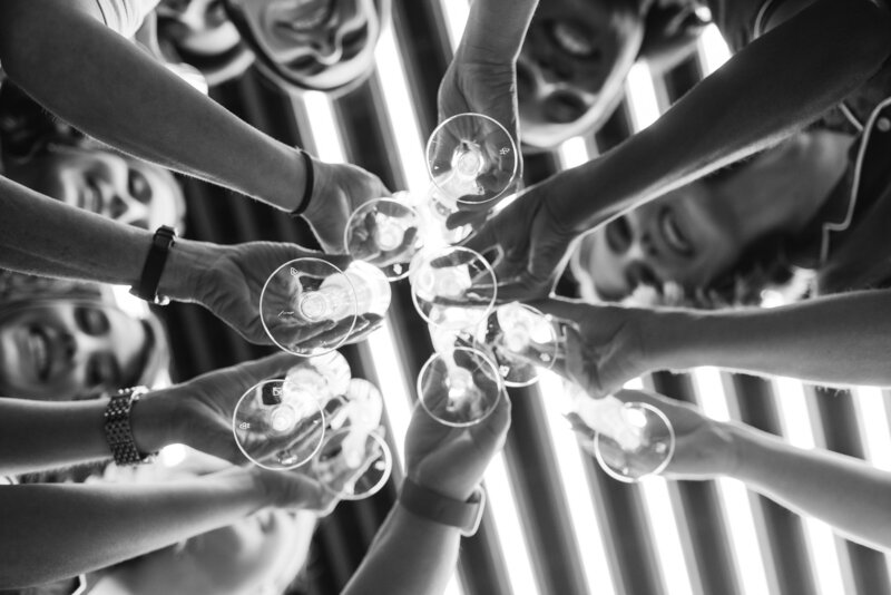 black and white of hands holding champagne flutes in a circle and clinking them