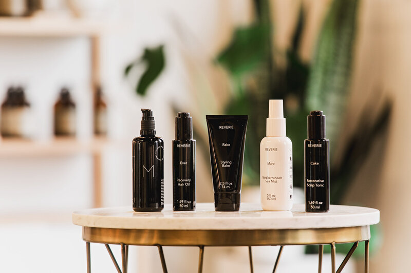A collection of Reverie hair products displayed on a round table representing eco hair products used at the The Collective Beauty and Wellness.