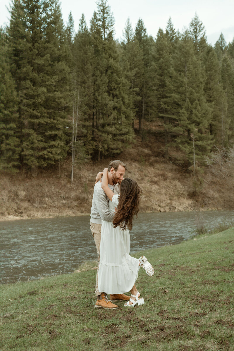 Photo of a girl and boy at their engagement session taken by Bailee Freeman Photography. Boy is embracing girl in a hug while they dance in front of pine trees in Ashton, Idaho. 