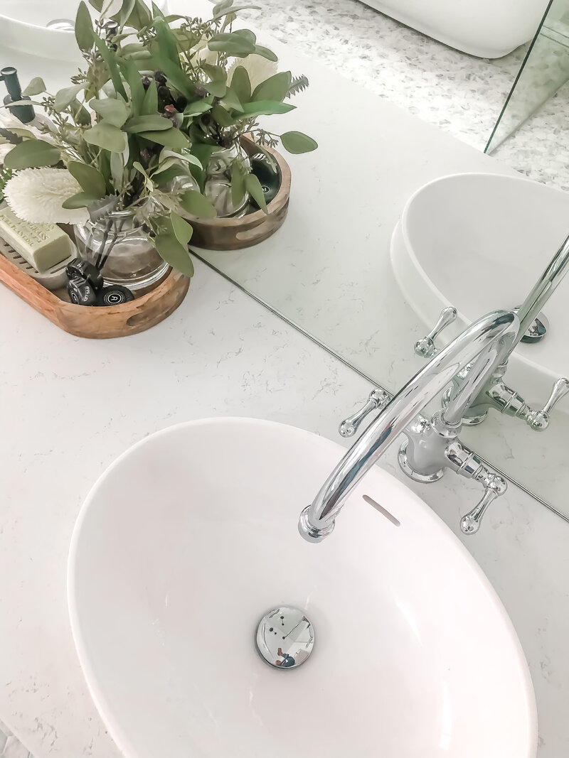 Bathroom sink with a chrome faucet and mirror; a wooden tray holds plants and toiletries nearby, exemplifying the elegance typical of full-service interior design in Newcastle.