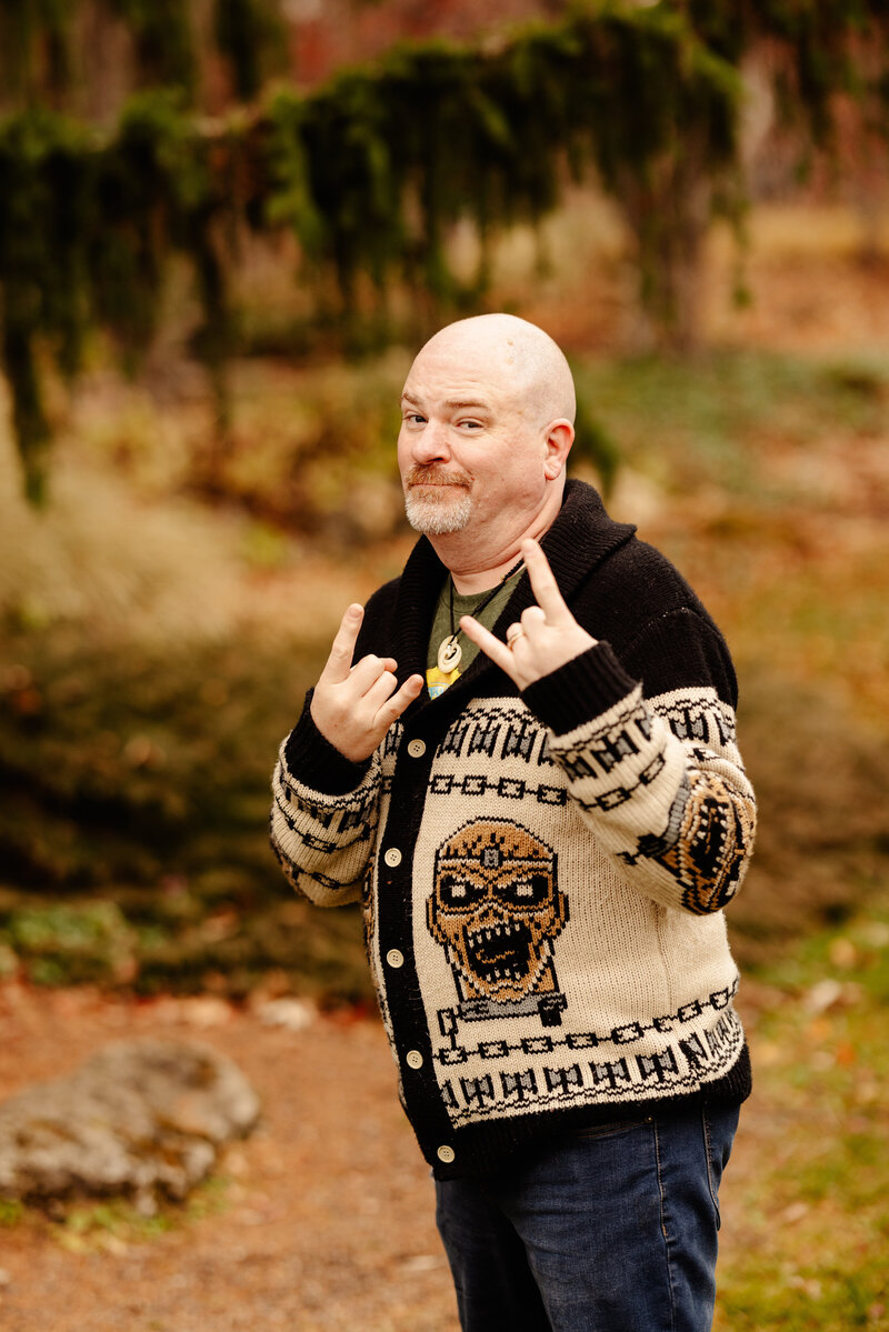 Man in sweater flashes heavy metal horns at the camera.