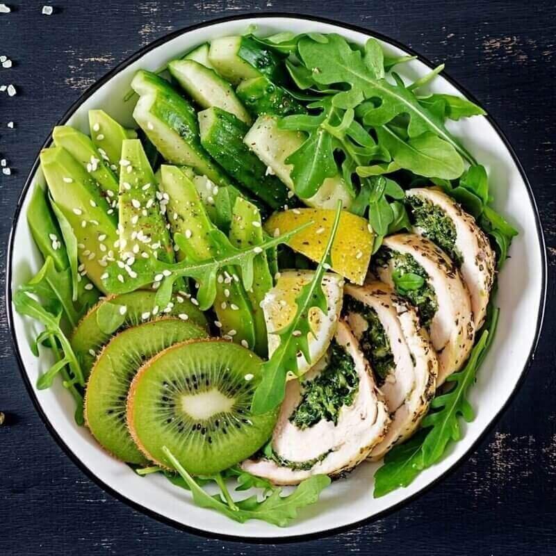 Healthy lunch bowl with fresh greens, kiwi, chicken, cucumbers and seeds.