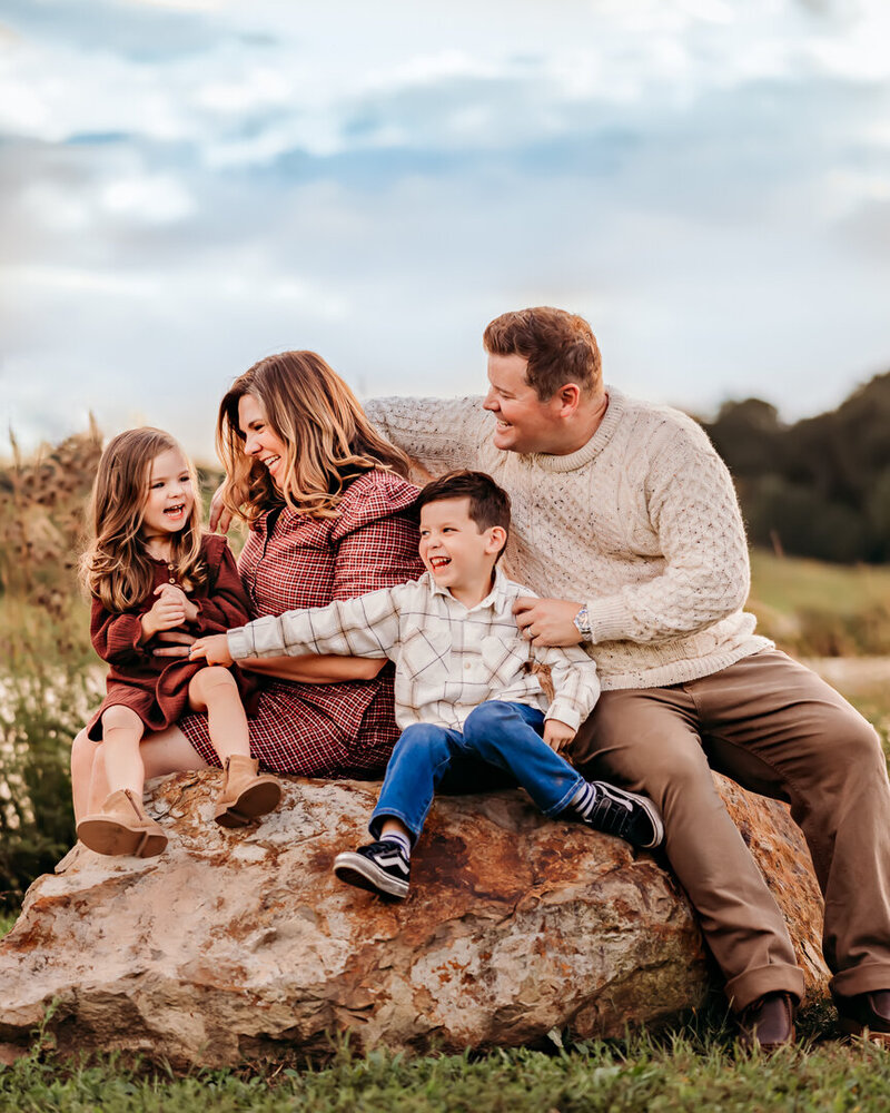 Family Photographer, a young family of four, with young son and daughter sit on a boulder outside