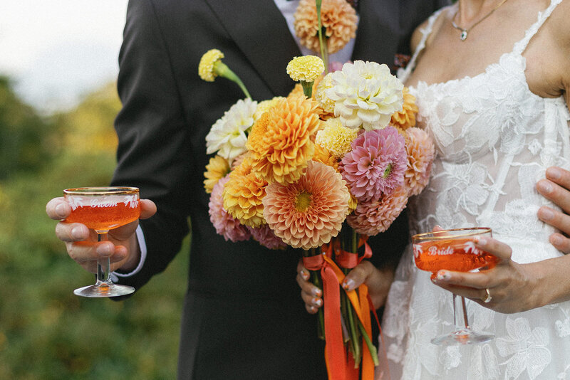 bride and groom holding custom cocktail glasses and a boquet while hugging