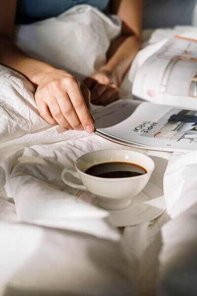 Man in bed reading a magazine with a cup of coffee