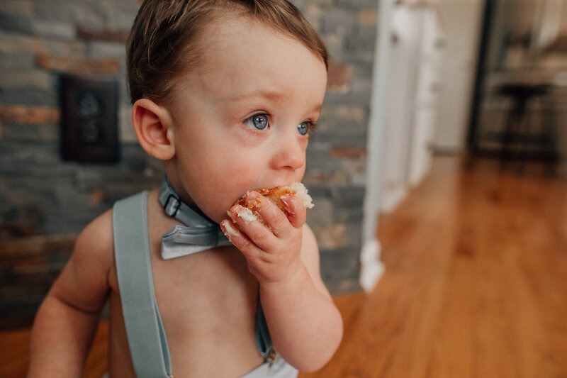Baby sits on the floor and eat birthday cake.
