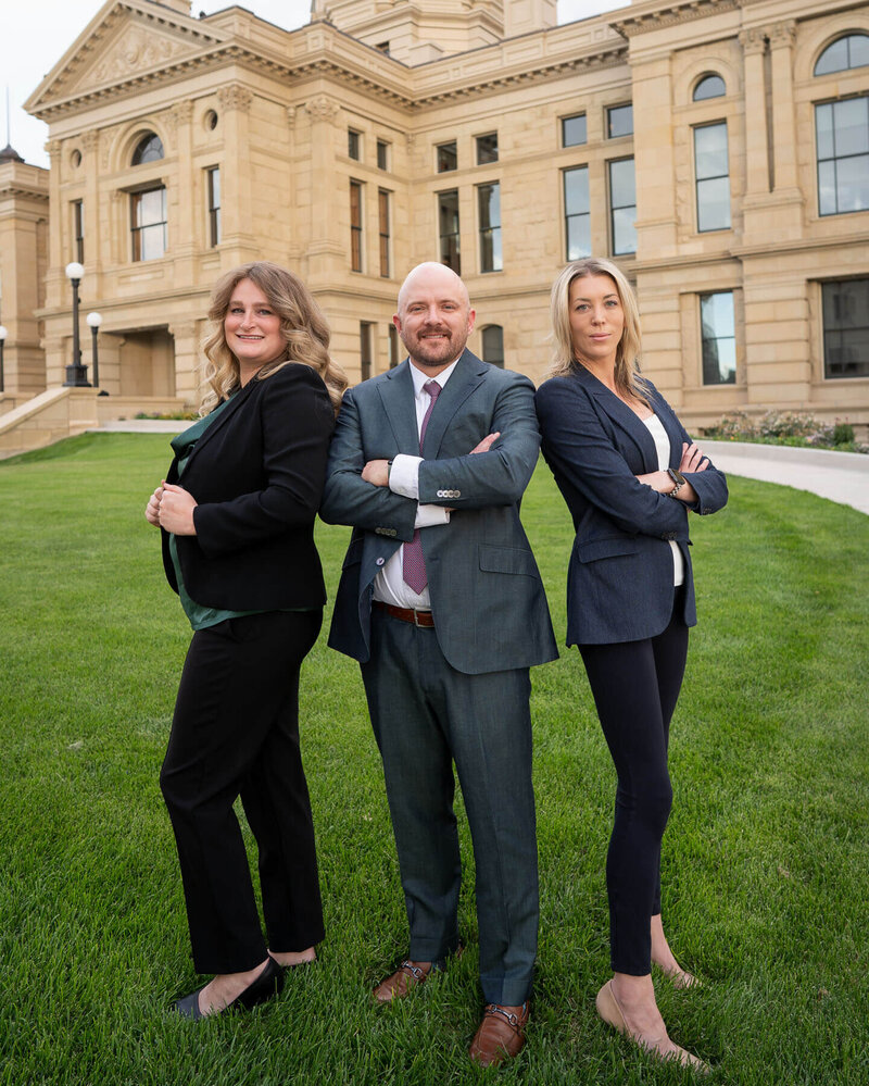 three cheyenne attorneys standing together on grass in front of wyoming state capitol dressed in business attire
