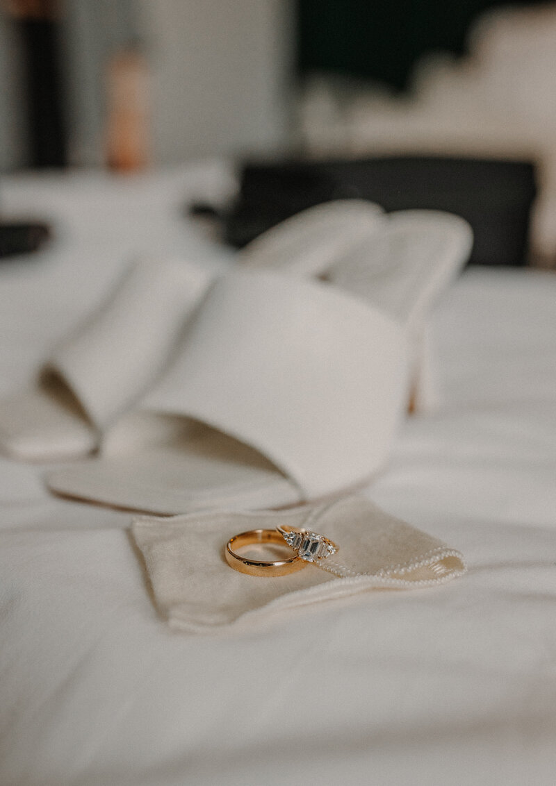 Gold rings resting on a bed with white heels