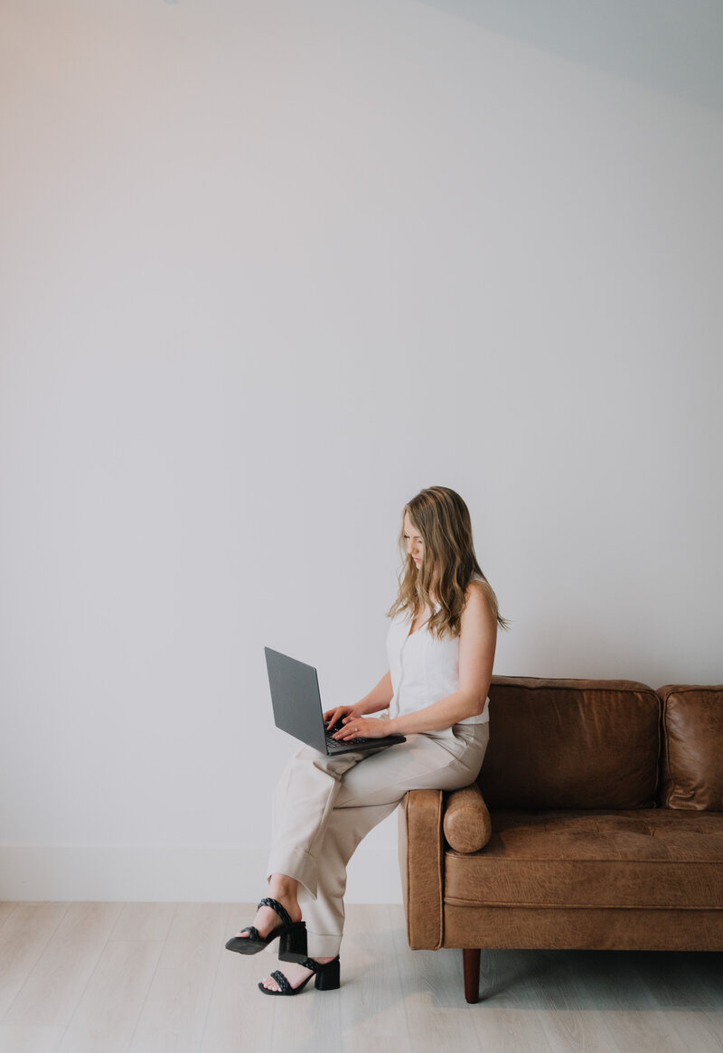 Megan sitting on the arm of a couch working on her laptop