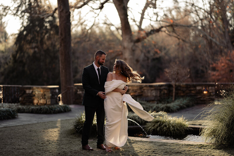 Bride and groom embracing from a twirl outside with the sun setting behind them with the bare winter trees.
