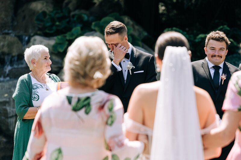 candid wedding photo of groom crying as bride walks down aisle in her backyard wedding