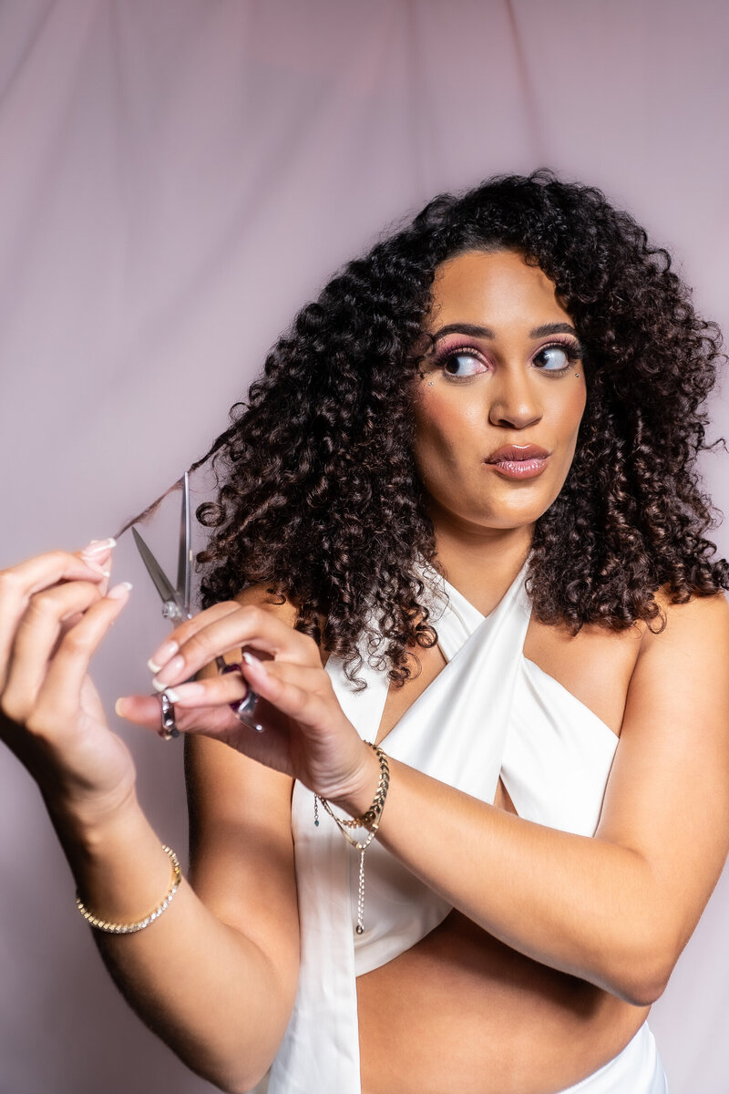 Woman with curly hair making a silly face while pretending to cut her hair.