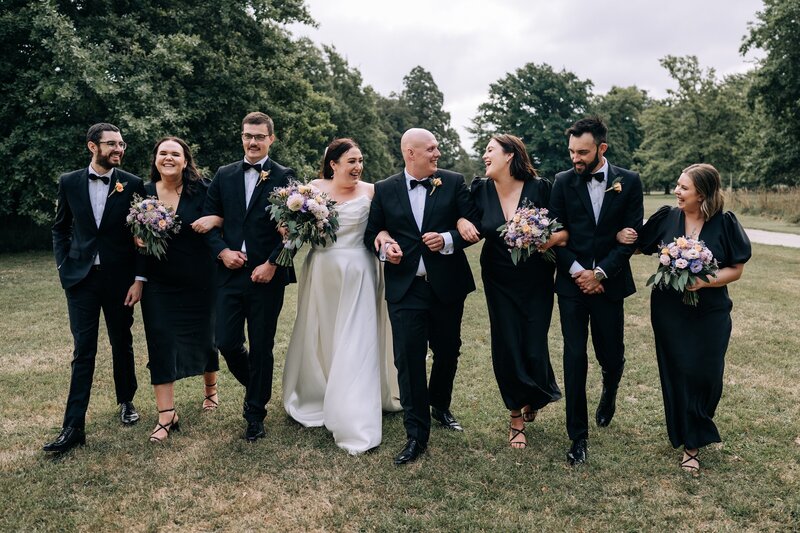 bridal party in black and white clothing walk together across grass at bangor farm wedding venue in darfield