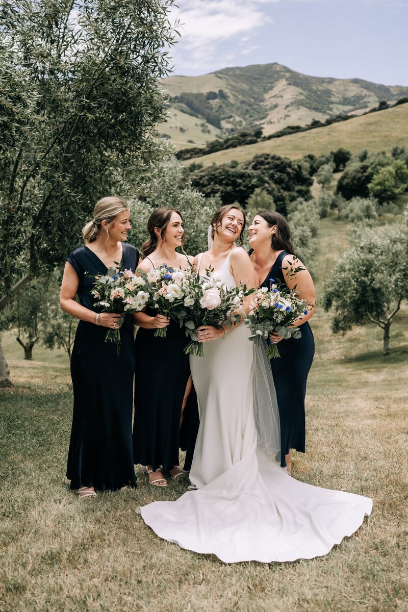 bridesmaids in black laugh with bride in akaroa olive grove on wedding day