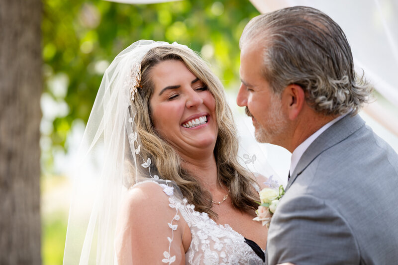 Bride laughing with her eyes closed as groom smiles at her.