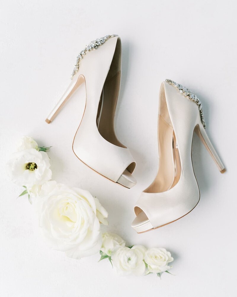 Elegant white bridal shoes with sparkling rhinestone details, artfully arranged with delicate white roses and flowers, reflecting refined wedding day details by a Virginia wedding florist.