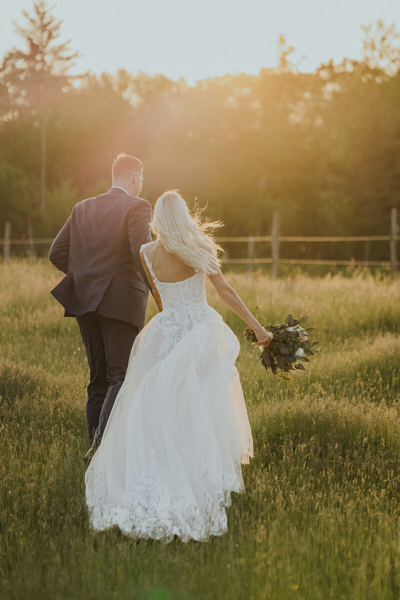 Bride and groom running hand in hand through a field at sunset on their wedding day.
