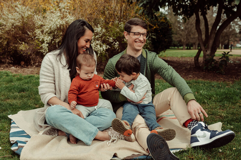 Family sitting in bed laughing with a newborn and toddler