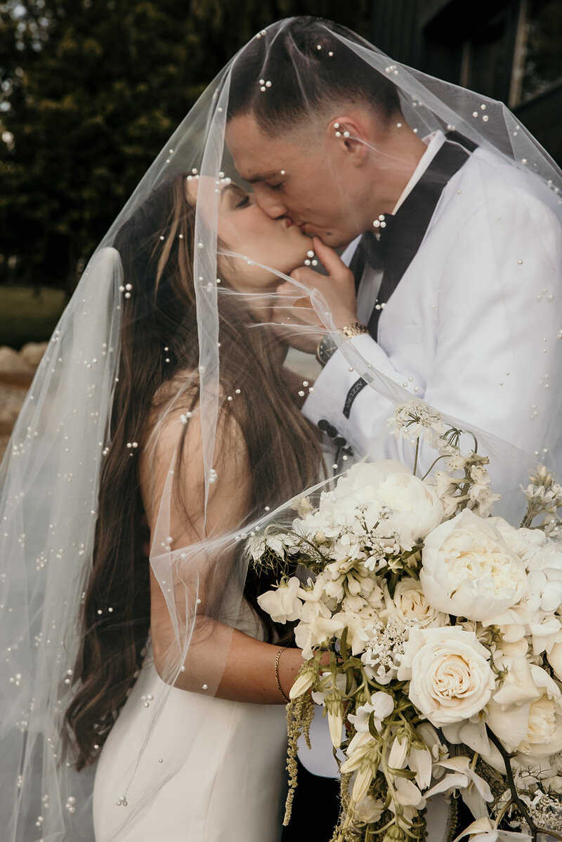 A newlywed couple share a kiss surrounded by friends holding sparklers.