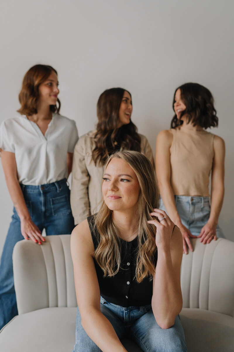 Megan sitting on a couch with her team members standing behind the couch
