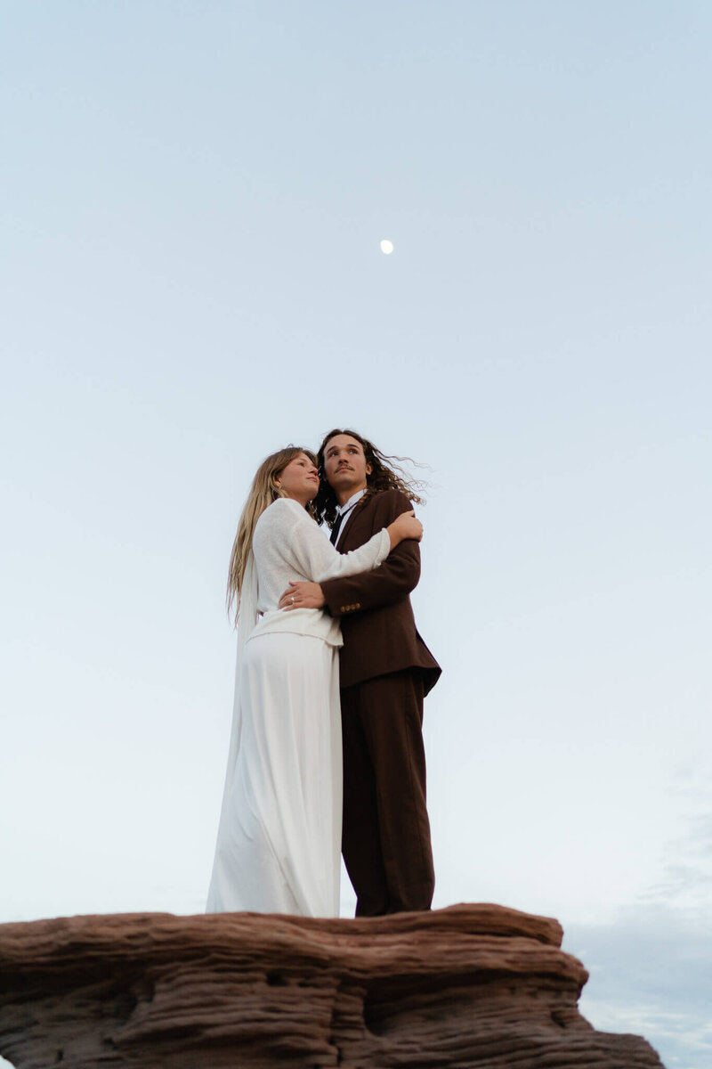 Couple sharing a quiet moment together in the Moab desert with the moon shining behind them after their elopement ceremony