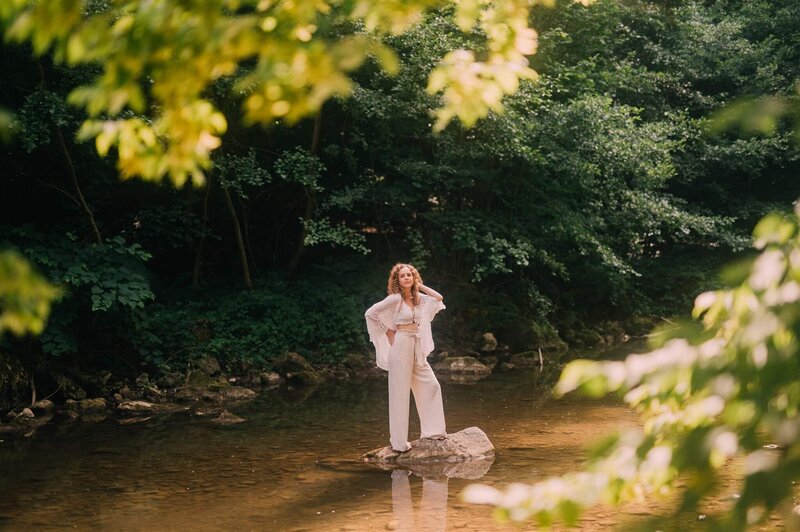 Frau steht auf einem Stein im Wasser in einem Waldstück