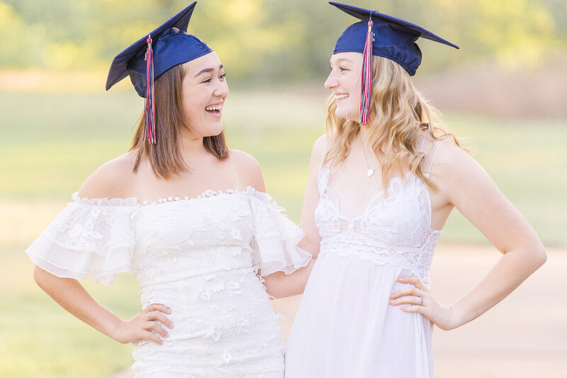 best friends wearing graduation hat looking at each other laughing during senior photographer in Ashburn, Virginia