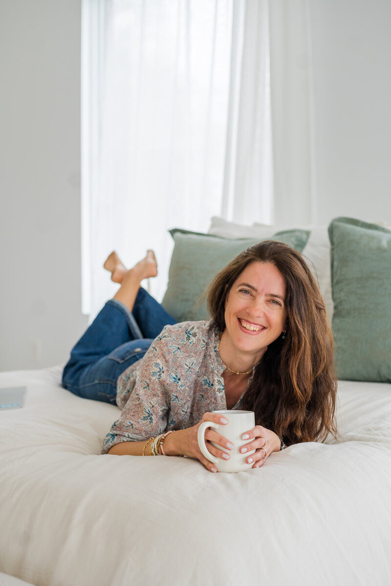 woman on a bed drinking coffee and smiling at the camera