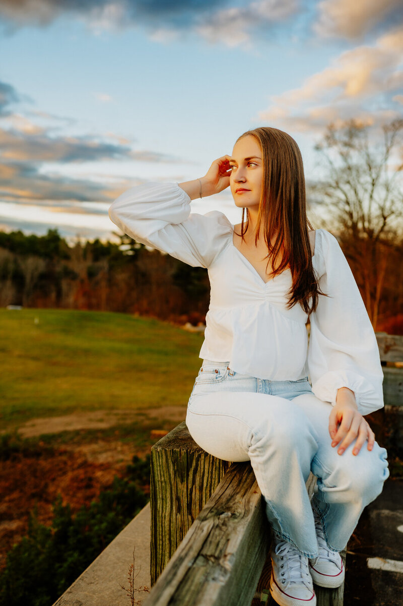 Girl sitting on a bench with her  hand on her head staring at the sun. 