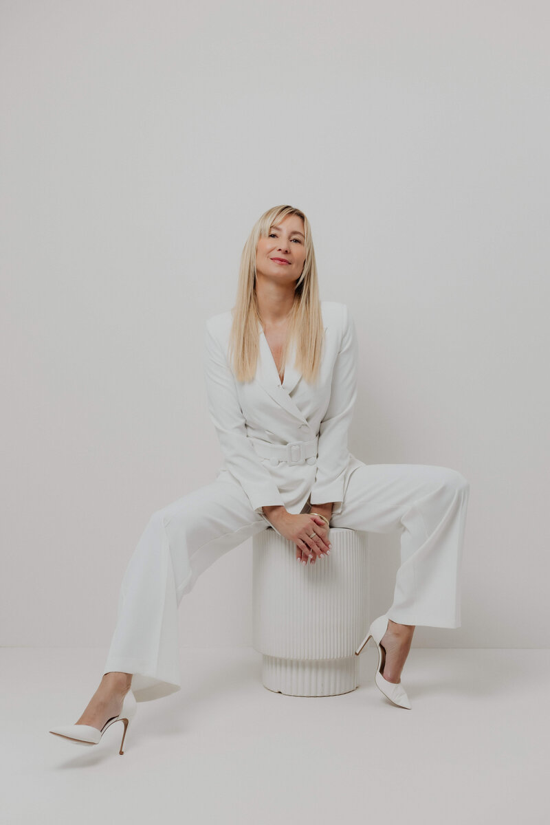 women in white suite sitting on a stool - exhibiting confidence.