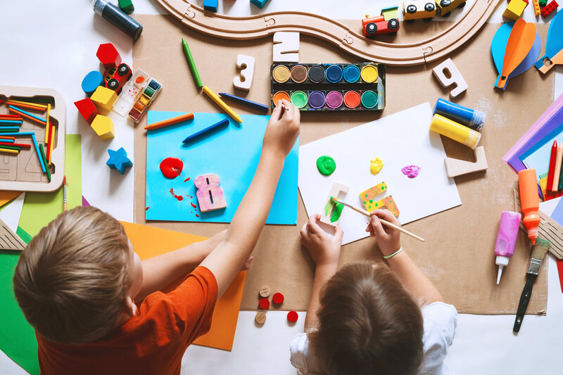 Aerial view of two children  painting wooden numbers with  bright colors in a play area
