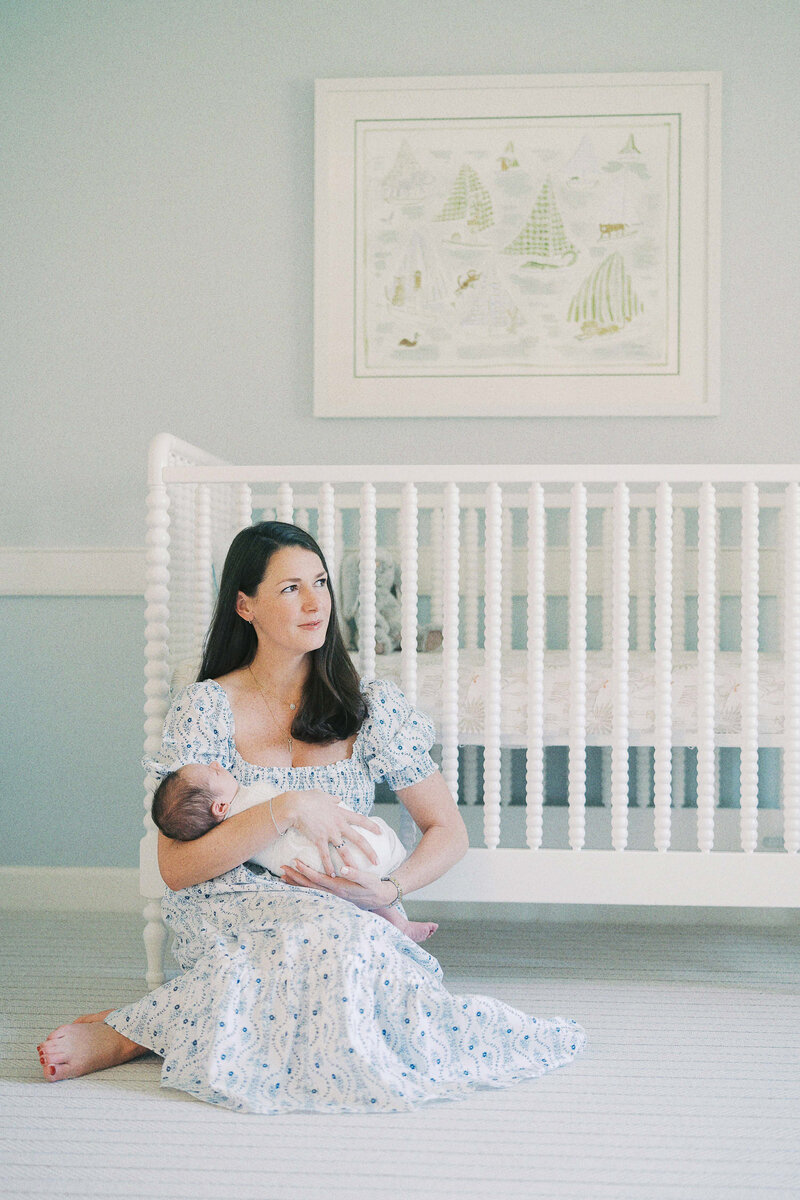 a woman holding her newborn baby while sitting by their crib