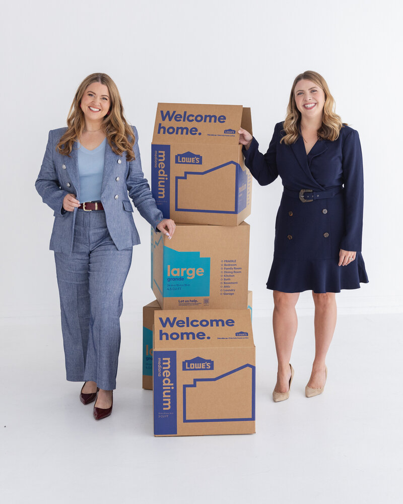 Keelie Luttrell and Brianna Castillo of Haven Realty Group smiling with moving boxes—representing their relocation concierge service helping clients move with confidence.