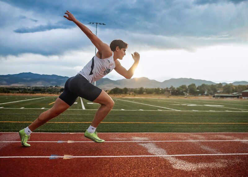 Senior guy posing at his high school track with his gear on.