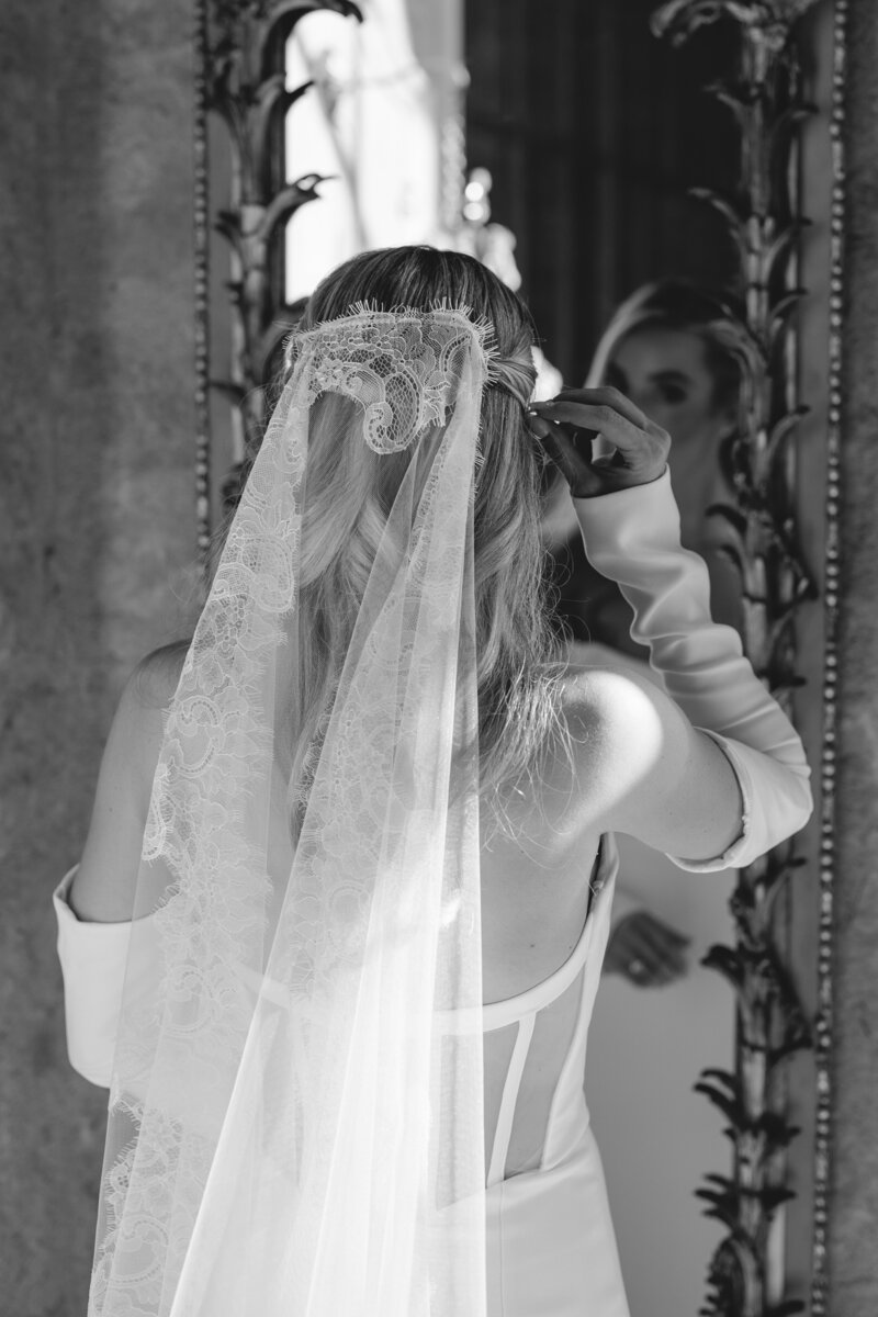 Black and white photo of  bride's bridesmaids helping adjust her hair and dress in front of an ornate window